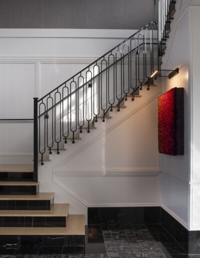 Modern staircase with black metal railings, light wooden steps, and a black-tiled floor. A vibrant red wall art piece hangs on the wall underneath the stairs.