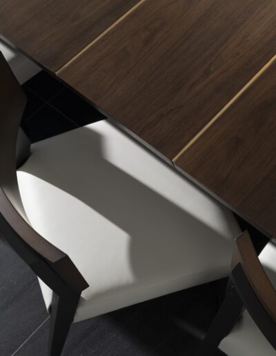 Top view of a dark wooden table with light-colored upholstered chairs underneath. Shadows are cast on the chairs, creating a contrast with the light and dark surfaces.