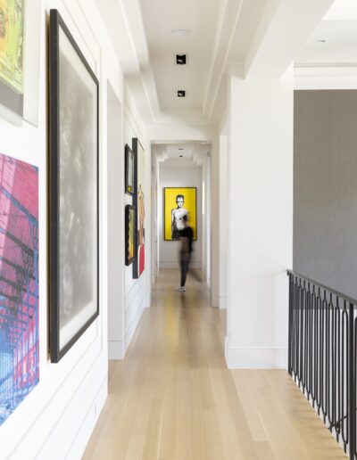 A person walks down a hallway decorated with various framed artworks, with a prominent yellow portrait visible at the end.