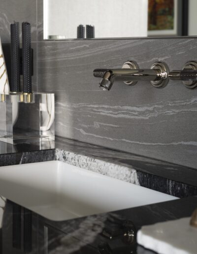Modern bathroom sink with a sleek faucet, a patterned vase, neatly stacked white towels, and a black and gray granite countertop.