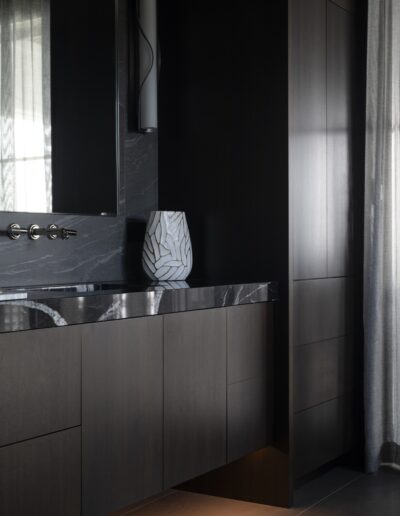 A modern bathroom features dark wood cabinets, a marble countertop with a unique vase, a wall-mounted mirror, and a grey curtain.