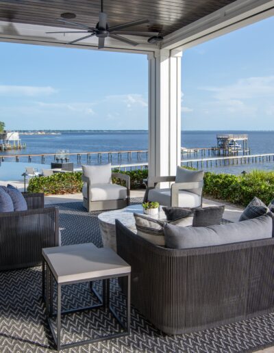 Spacious outdoor patio with modern furniture, overlooking a scenic waterfront with a dock and blue sky in the background.